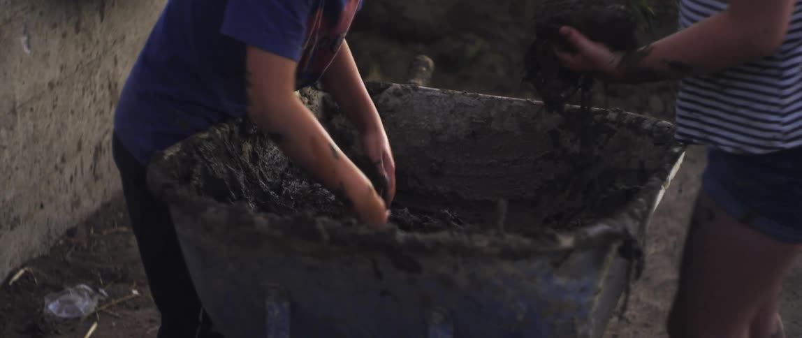 People pulling slimy black stuff from a wheelbarrow