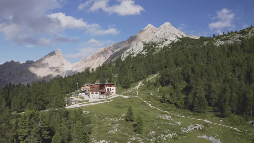 Aerial view of house on mountain slope surrounded by trees with mountains in the background