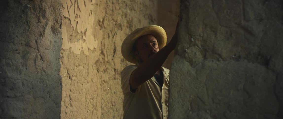 A man rubs his hands over a smoothed stone wall within a larger structure