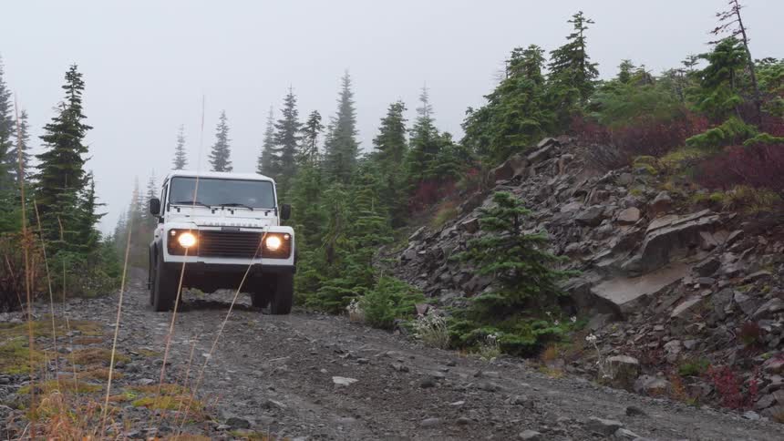 White land rover with headlights on driving on a rural road on an overcast day