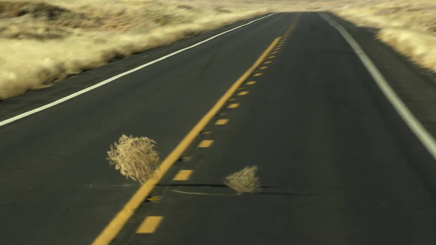 Tumbleweed rolling across the road with a landscape the sky and clouds in the background