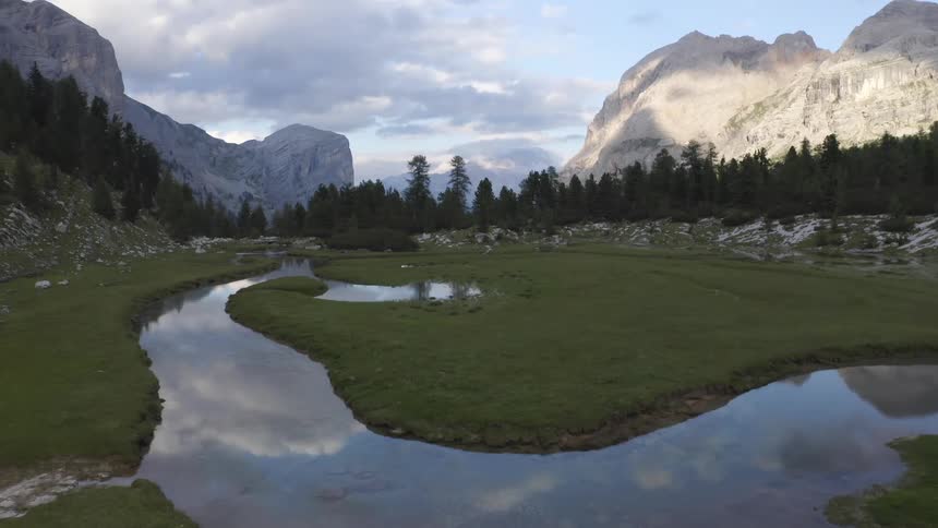 Stream runs through a field as mountains sit nearby under a cloudy sky