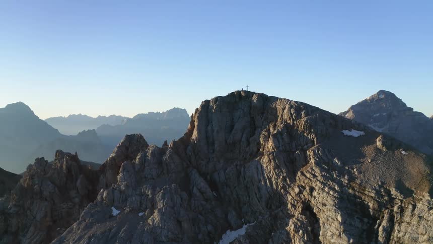 A mountain ridge with a cross erected on the summit under a clear blue sky