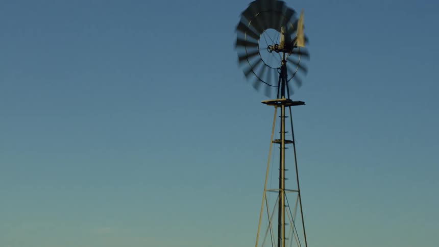 A windmill at the base of a hill blows in the wind