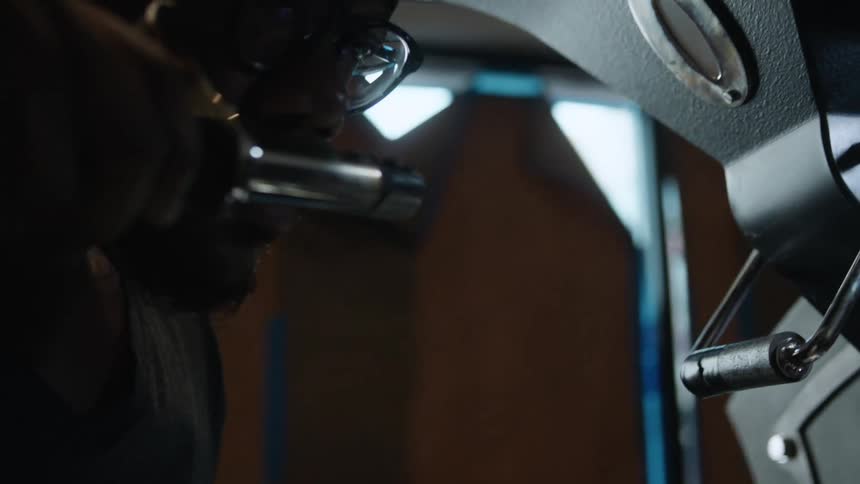A man with glasses in a room taking beams from a machine and smelling it with a wall and window in the background