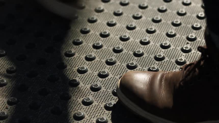The feet of people as they walk across a metal grate