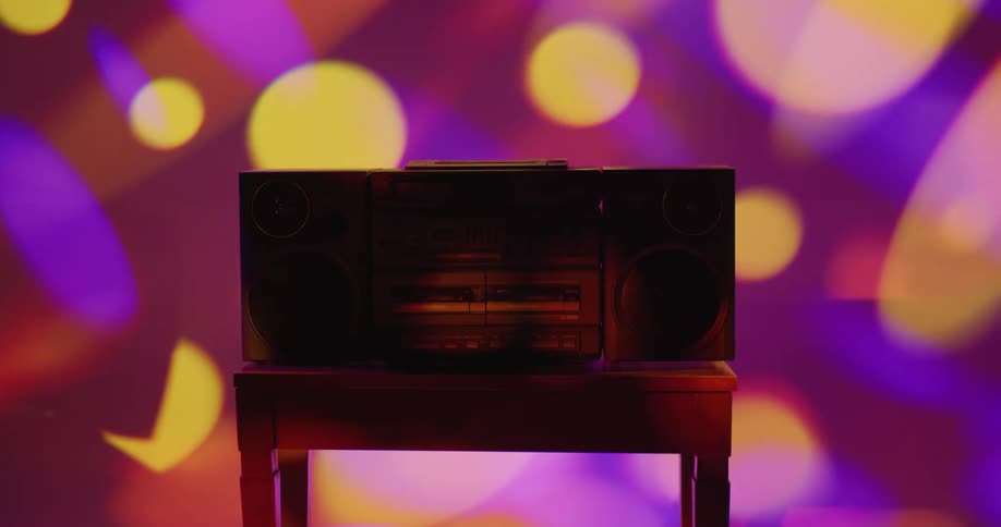 Colorful lights flash around a room where a boom box sits on a small table