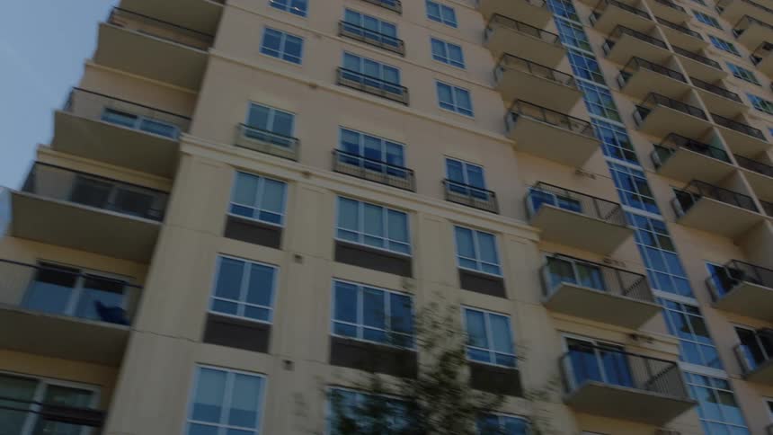 Cars sit parked on street next to apartment build with balconies under clear blue sky