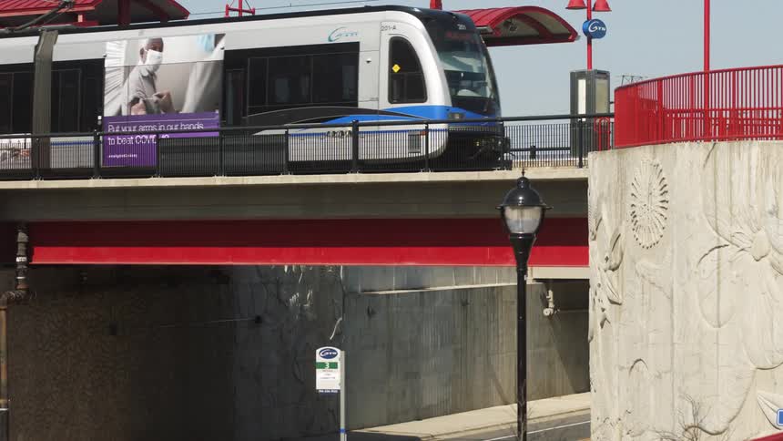 Light rail train with picture of person wearing face mask on the side pulls up to transit station