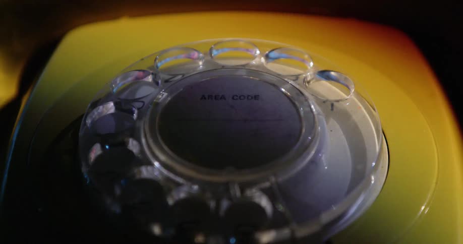 An older style rotary dial phone has its dial turn as lights shine upon it
