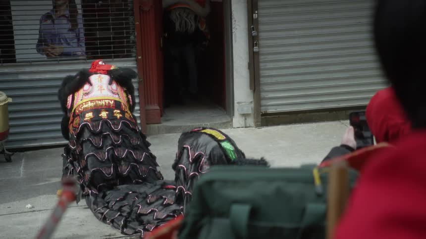 A person plays the drum while people in costume perform a dragon dance in the city