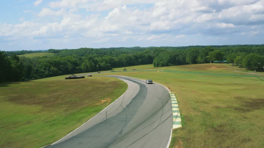 Vehicles racing on a racetrack with trees the sky and clouds in the background