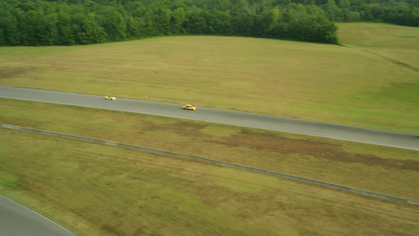Race cars speed down a straightaway and into a corner on a race track in a large field during the day