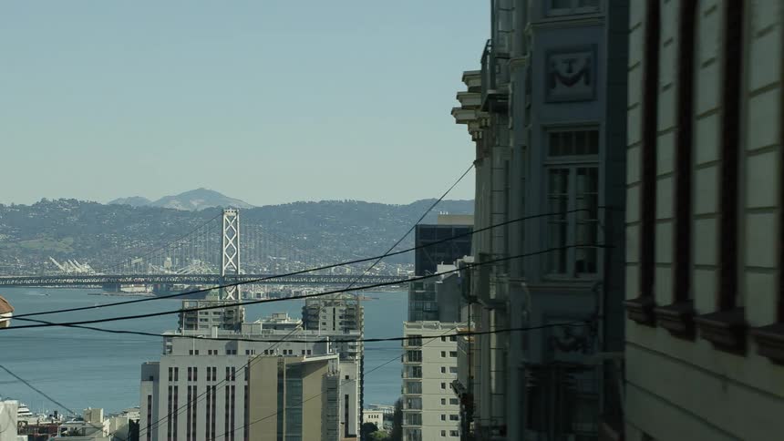 Cable lines sit high above a road connected tall buildings along the coast in a city