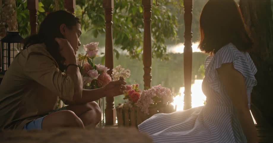 Two women sit on a patio overlooking the water while on holds some small flowers