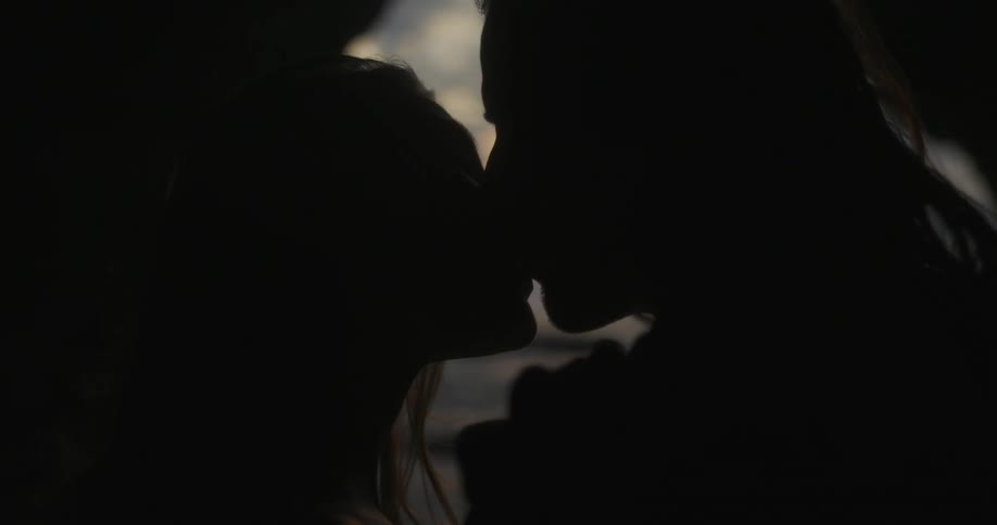 A man and woman kiss in a cave on the coast at sunset