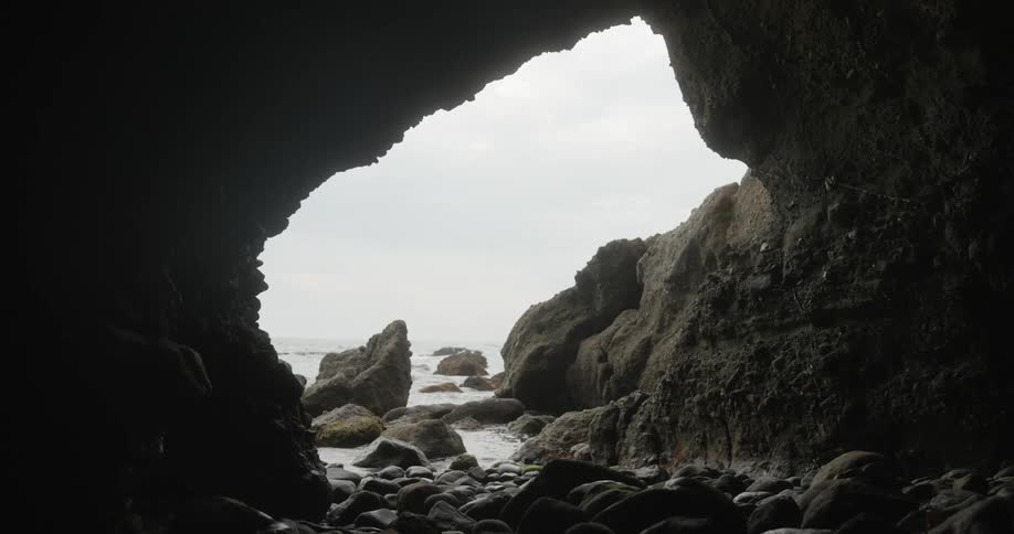 From the inside of a rocky cave a body of water can be seen