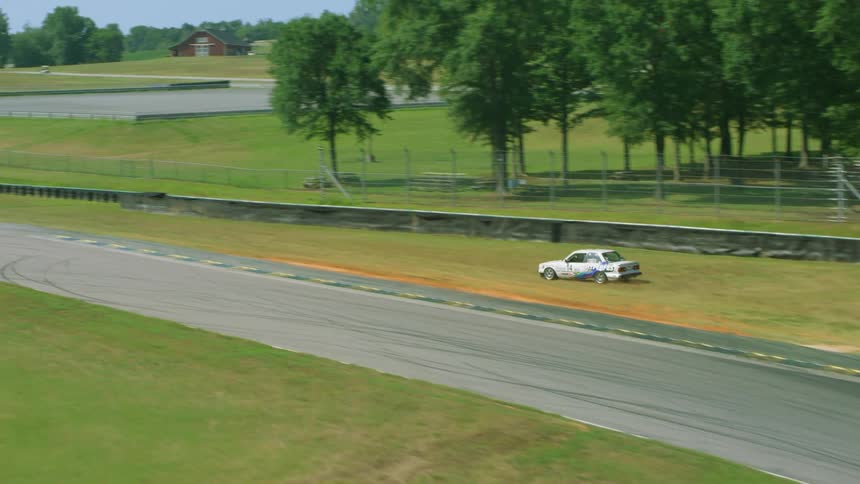 Race car drives off track into field before driving back onto track to follow other race cars