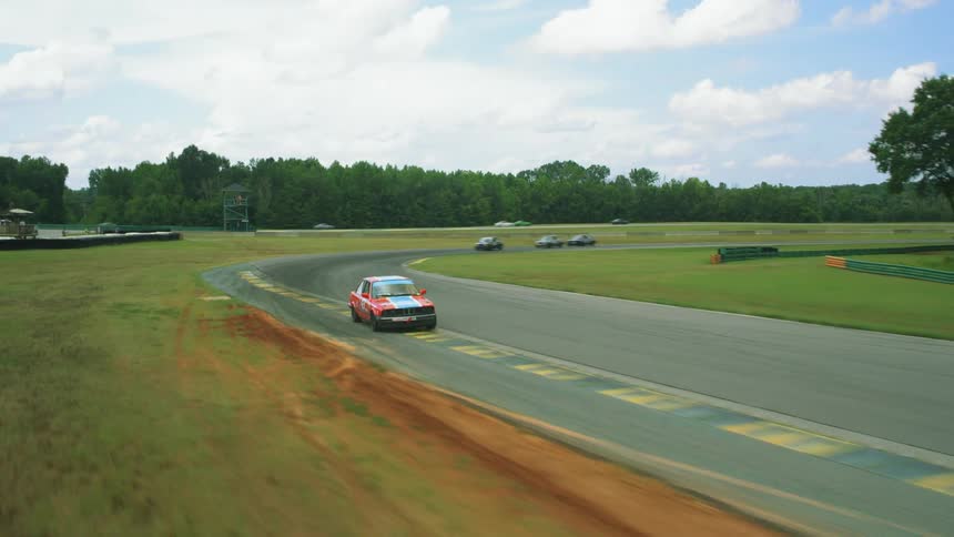 Races cars turn a corner on a race track outdoors during the day