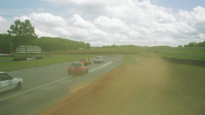 Vehicles racing on a racetrack with trees the sky and clouds in the background