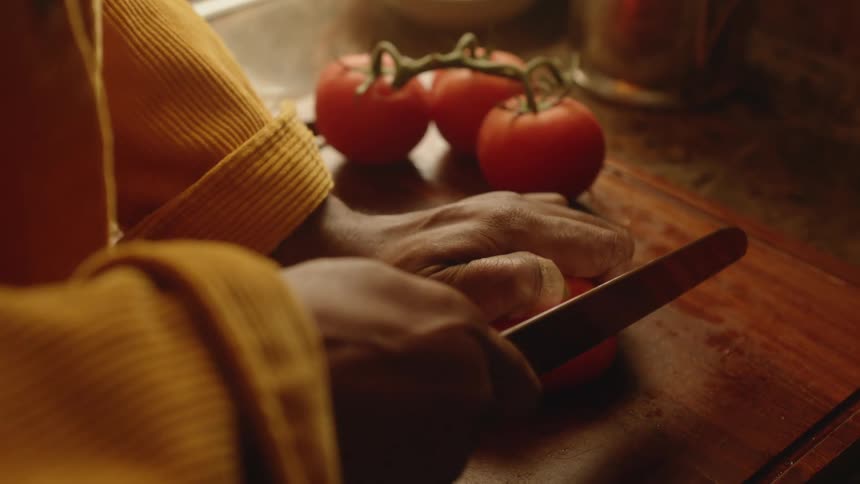 A man struggles to cut a tomato and squeezes it in frustration