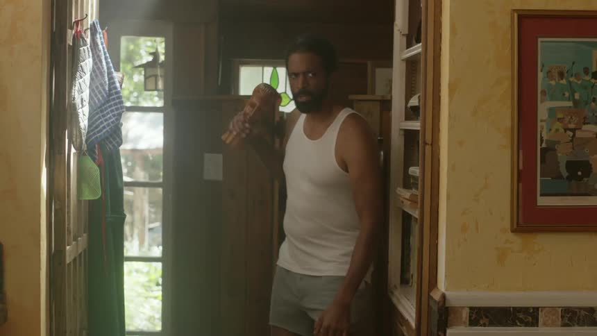 Man wearing underwear carries a blunt object while walking cautiously at home