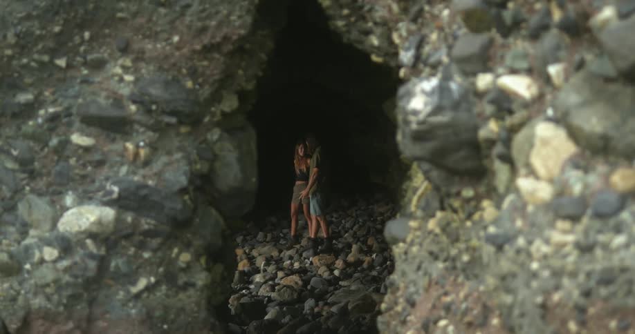 Man wearing boots shorts and t shirt and woman in shorts and sleeveless shirt stand on stones in dark cave