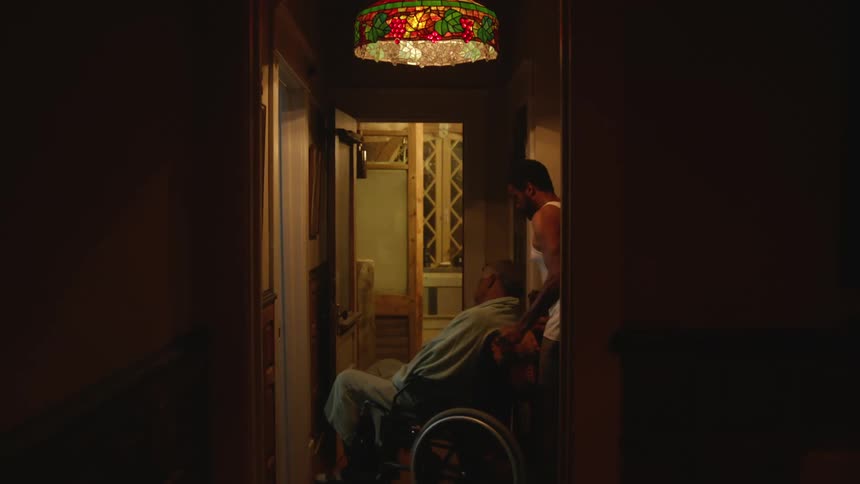 Man with undershirt and shorts pushes disabled old man