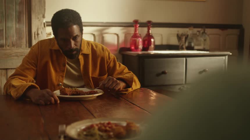 A man silently eats his food while someone else watches