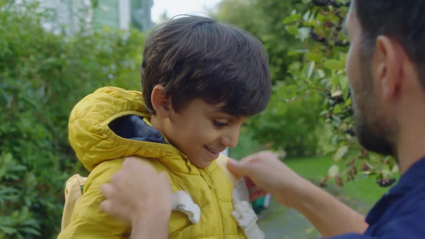A father helps his son put on his backpack