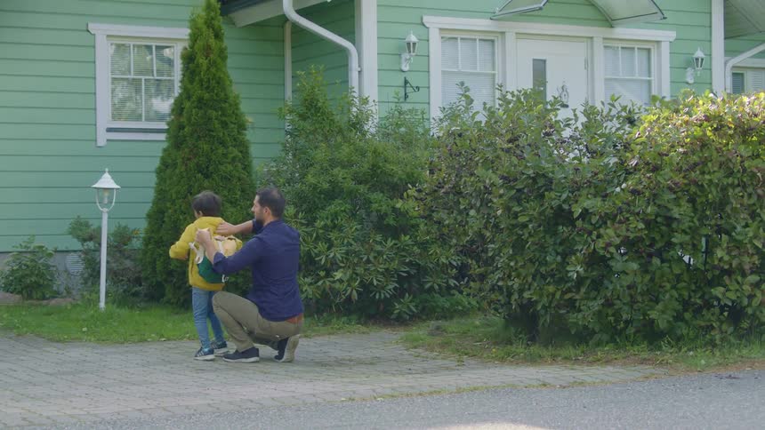 A father is crouched down to help his son put on a backpack