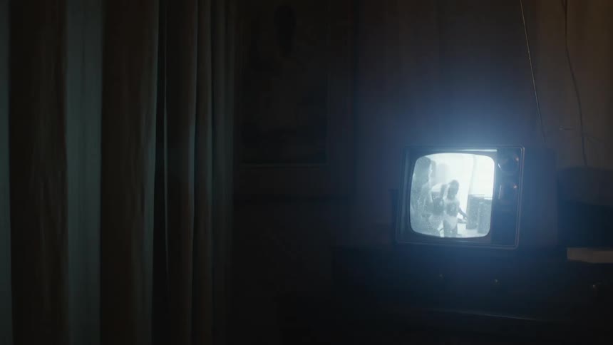 A man in a room with a blackandwhite television with curtains and a wall in the background