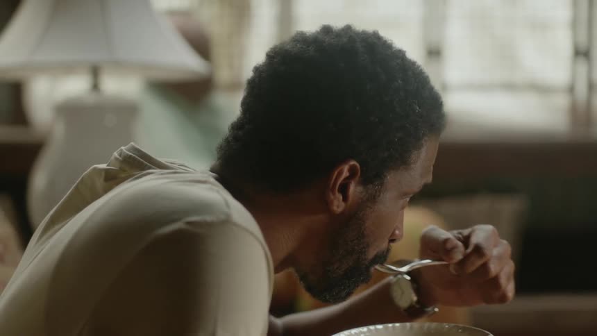 Young man sitting in a chair eating and watching television while taking care of an senior citizen at home