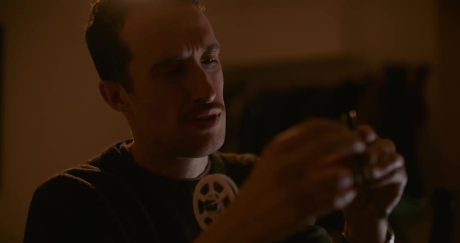 Man sitting in dimly lit room near laptopthreads film onto reel before attaching it to film projector