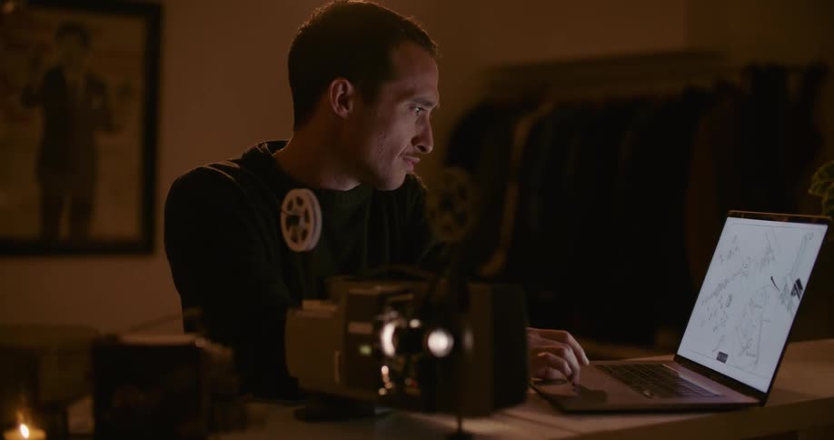 A man in a room using a laptop and adjusting a projector with a wall in the background