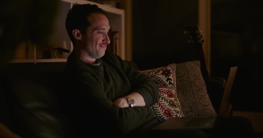A man laughs while watching a video on his laptop