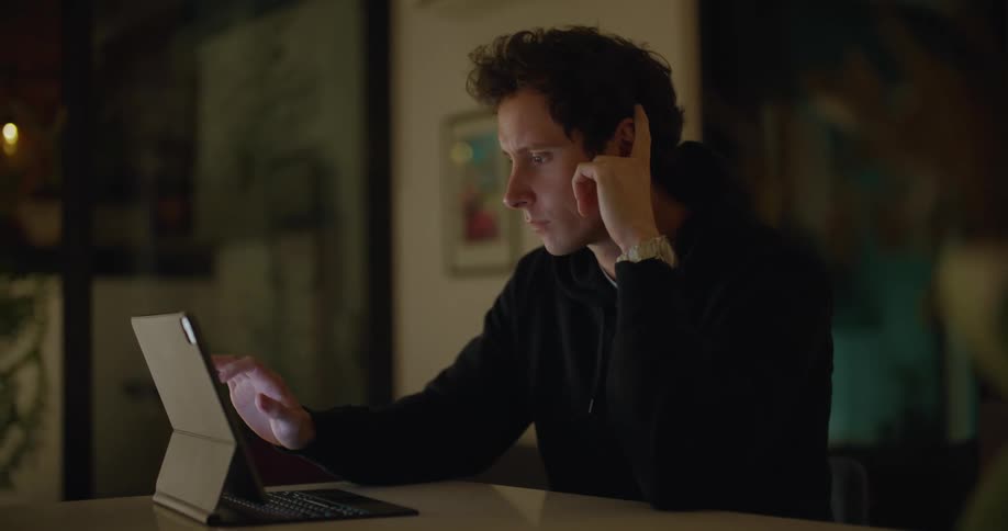 A man in a room using a tablet on a table with a wall in the background