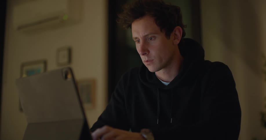 A man uses his tablet as a laptop while sitting at a desk at home
