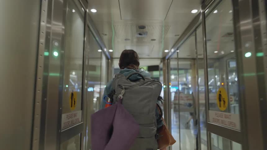 Woman walks through glass doors at airport terminal carrying backpack