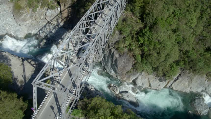 A pickup truck with a trailer crosses a bridge over a flowing river