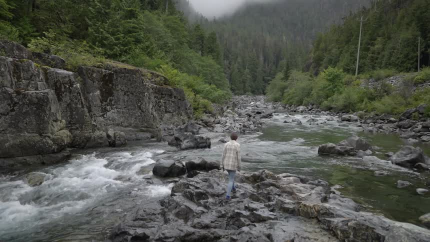 A woman is hiking on rocks near a river in a forest