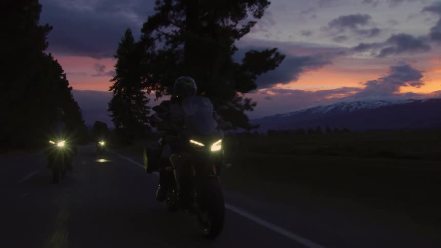 People are riding motorcycles at dusk on a remote mountain road