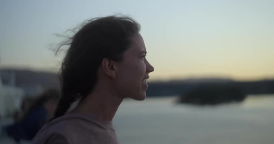 A woman looks out over the ocean while standing on the coast on a windy evening