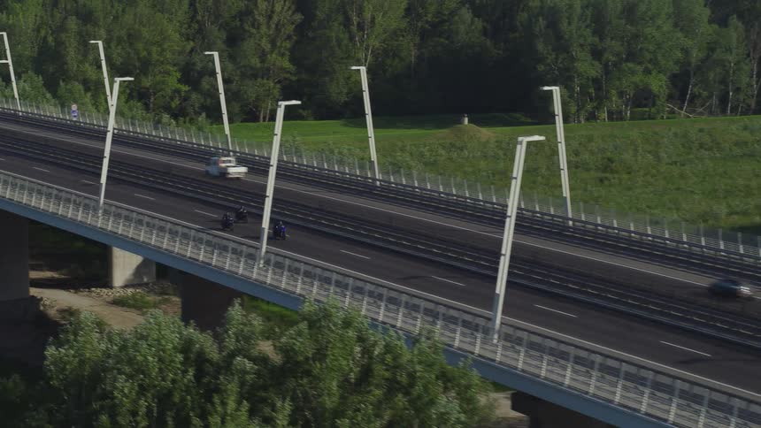 Motoryclists ride in a group together speeding down a bridge over a river