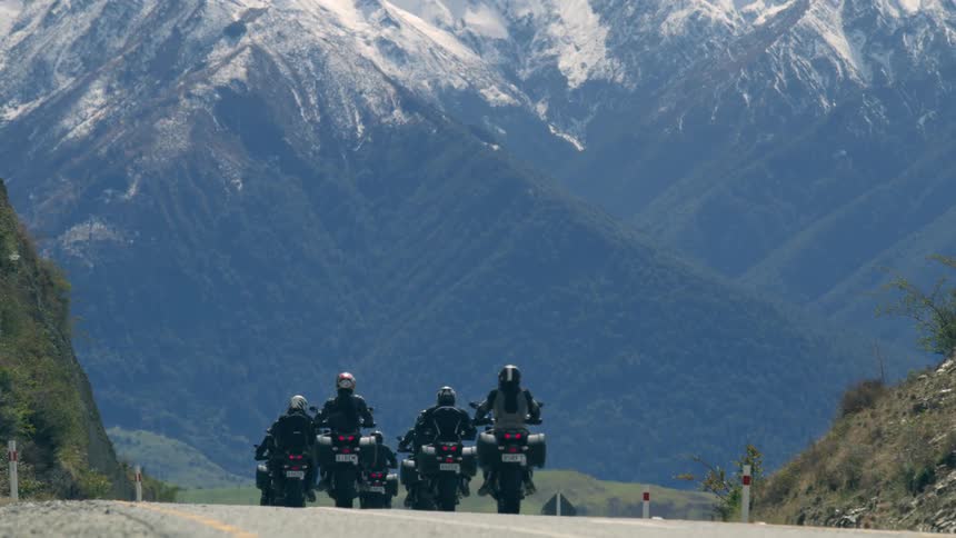 A small group of people ride motorcycles on a quiet road with mountains in the distance