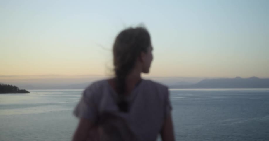 A woman looks out over the ocean as wind whips through her clothing and hair