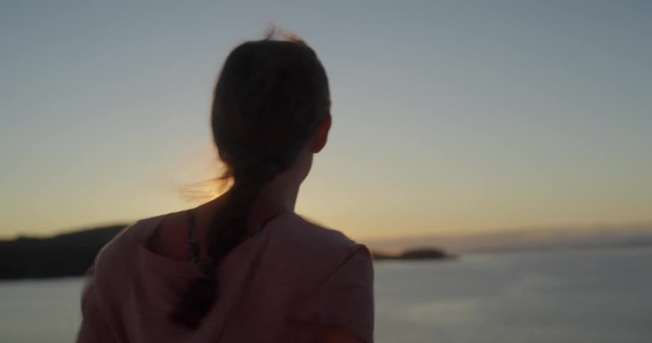 Woman with ponytail and shirt watches sunset smiling while traveling on ferry boat