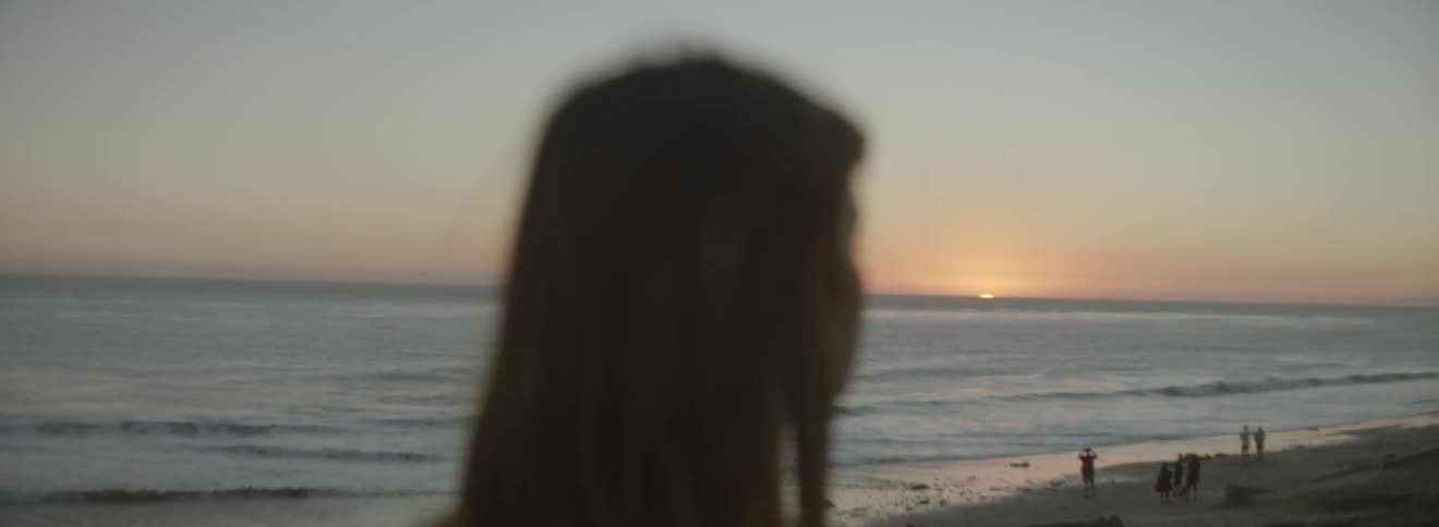 A woman is standing on the beach at sunset