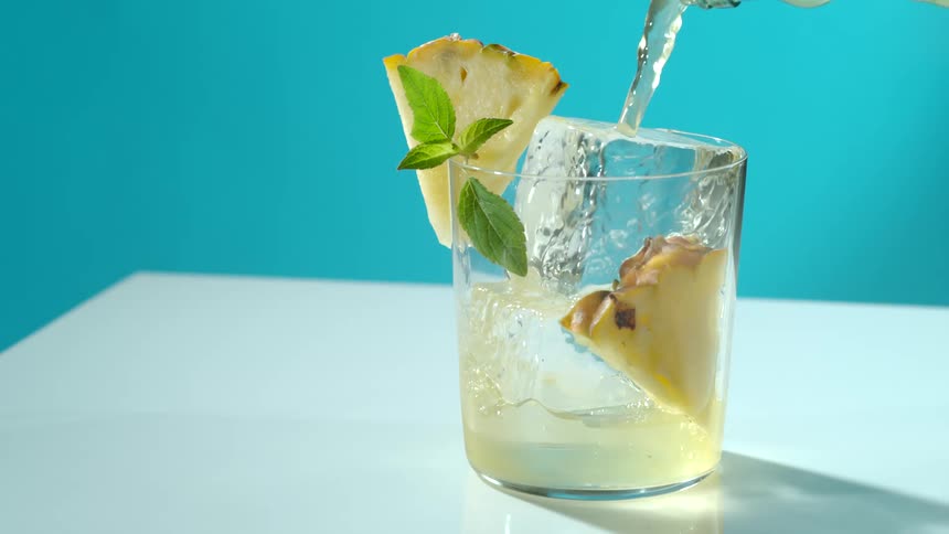 Liquid pours into a clear glass garnished with pineapple wedge and mint leaves