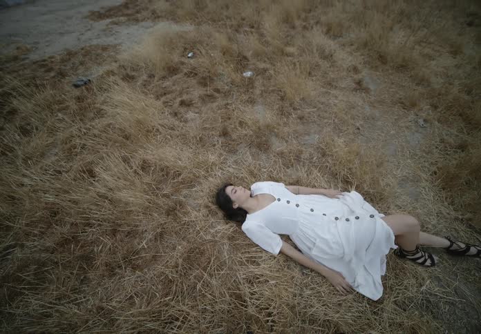 Woman wearing a white dress resting on the ground over the yellow dry grass on the hill